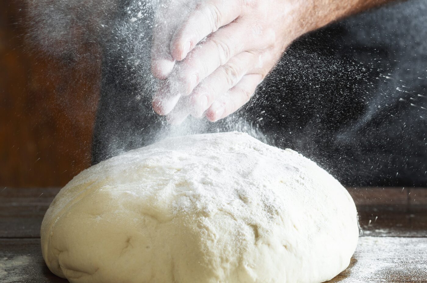 Hand bestäubt Teig mit Mehl auf Holzfläche — echtes Bäckerhandwerk